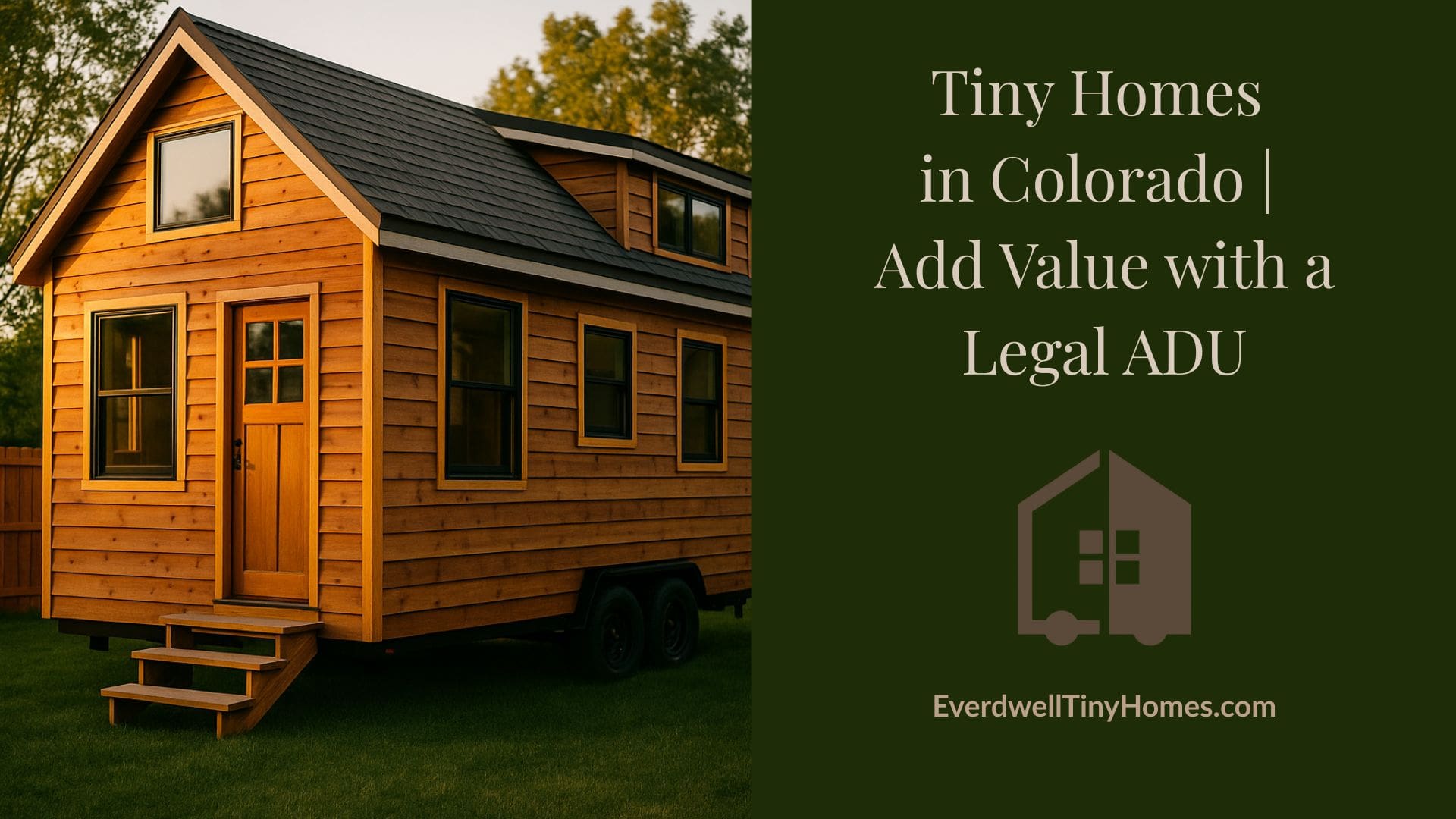 A cozy modern tiny house with wood siding and large windows, nestled next to a main residential home with a well-kept lawn and mountain views in the background.